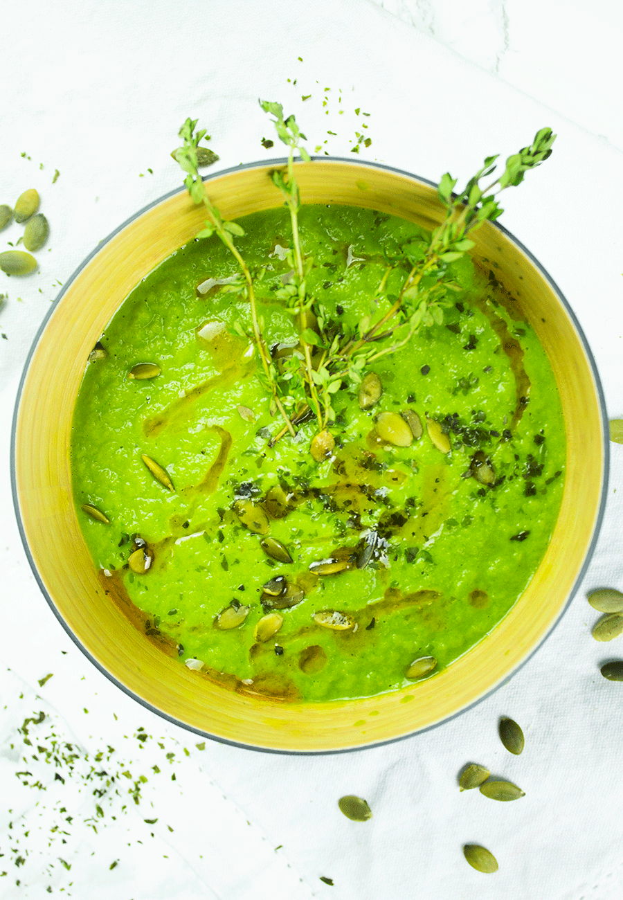 Warm green immune-boosting soup in a bowl, garnished with herbs and pumpkin seeds