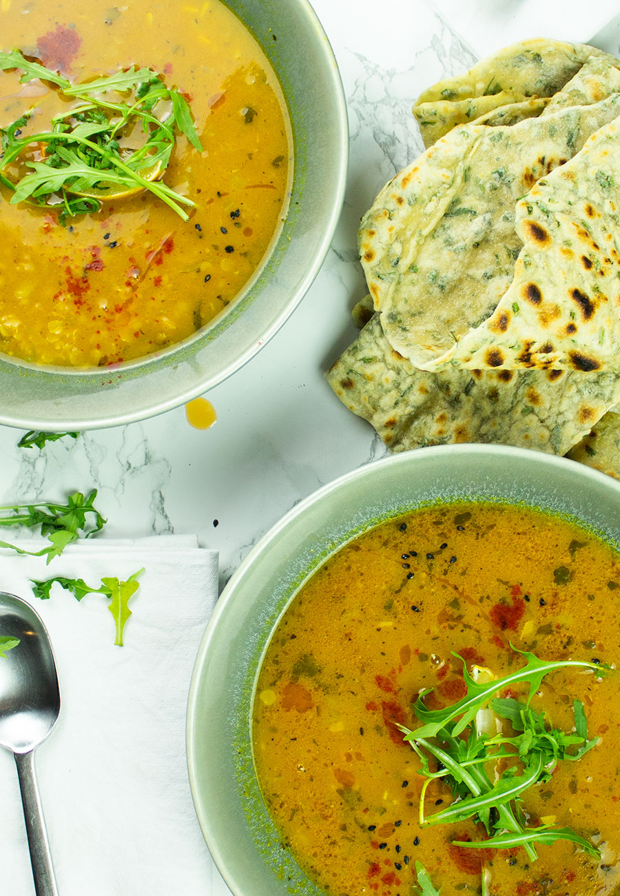 Hearty Indian dahl red lentil soup in bowls with flatbreads on the side 