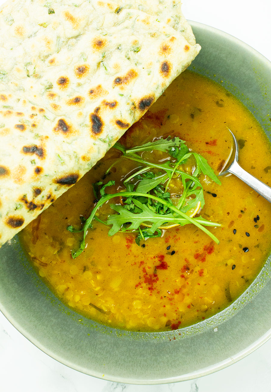 Dahl soup in a bowl with flatbreads on top of the bowl